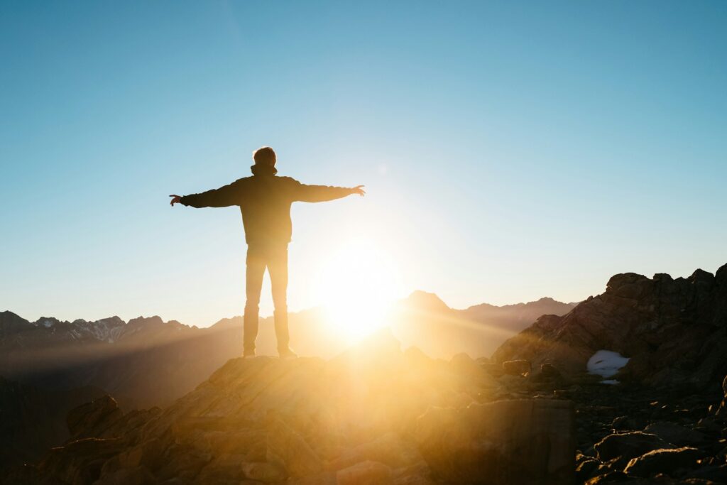 Silhouette of a person standing on a mountain peak at sunrise with arms outstretched, symbolizing financial freedom and reaching a debt-free milestone in 2026.